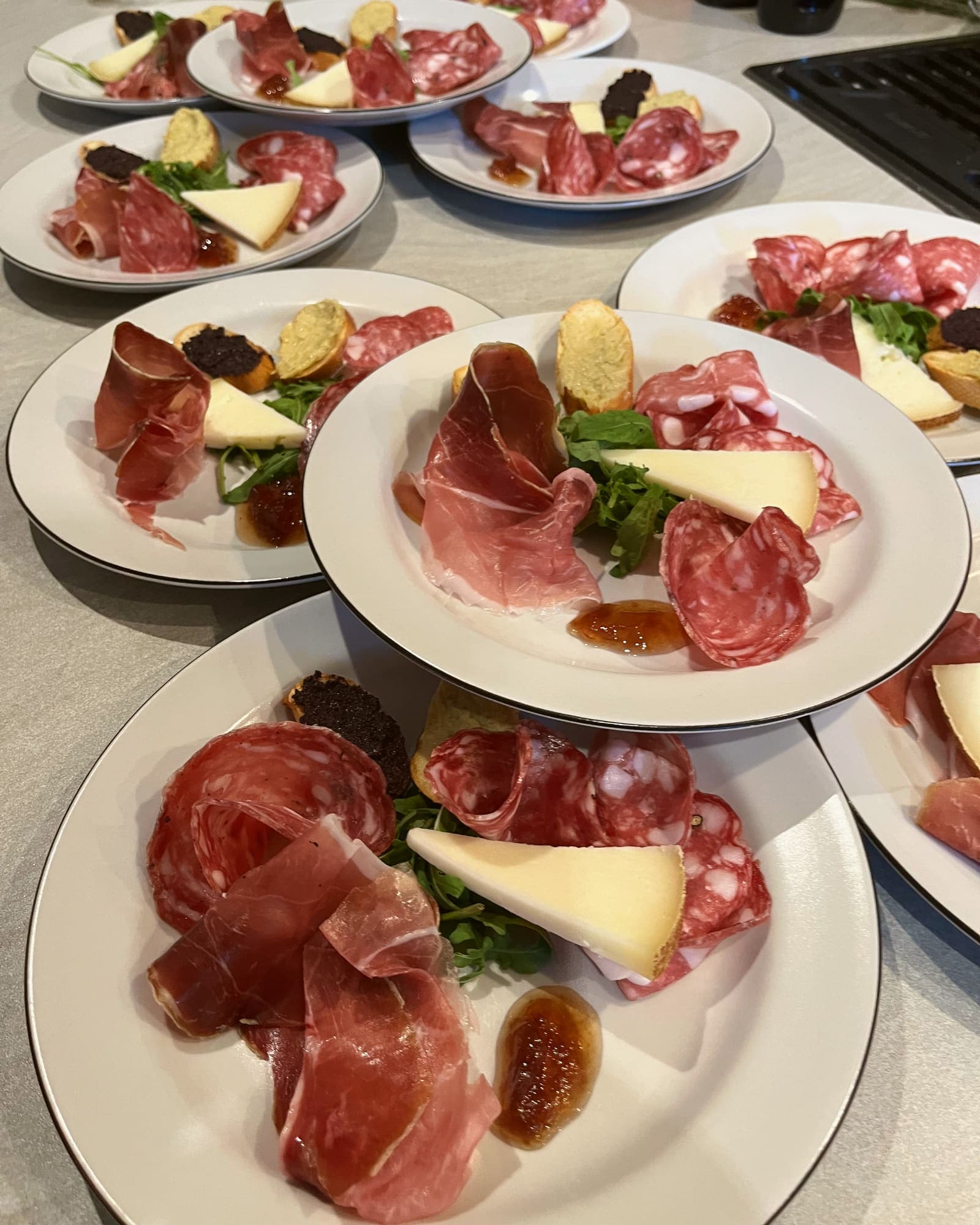 Plates of cured meats, a wedge of pecorino and crostini, set out on a kitchen counter before dinner.