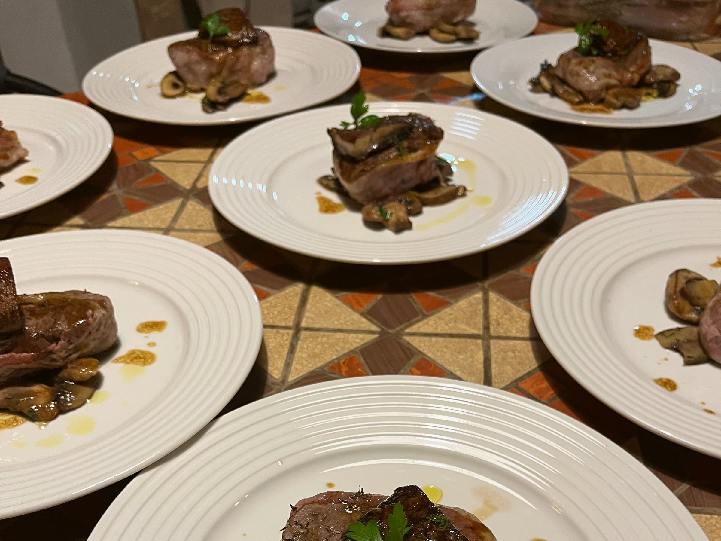 Seared rounds of beef on mushrooms, plated side by side on a tiled table.