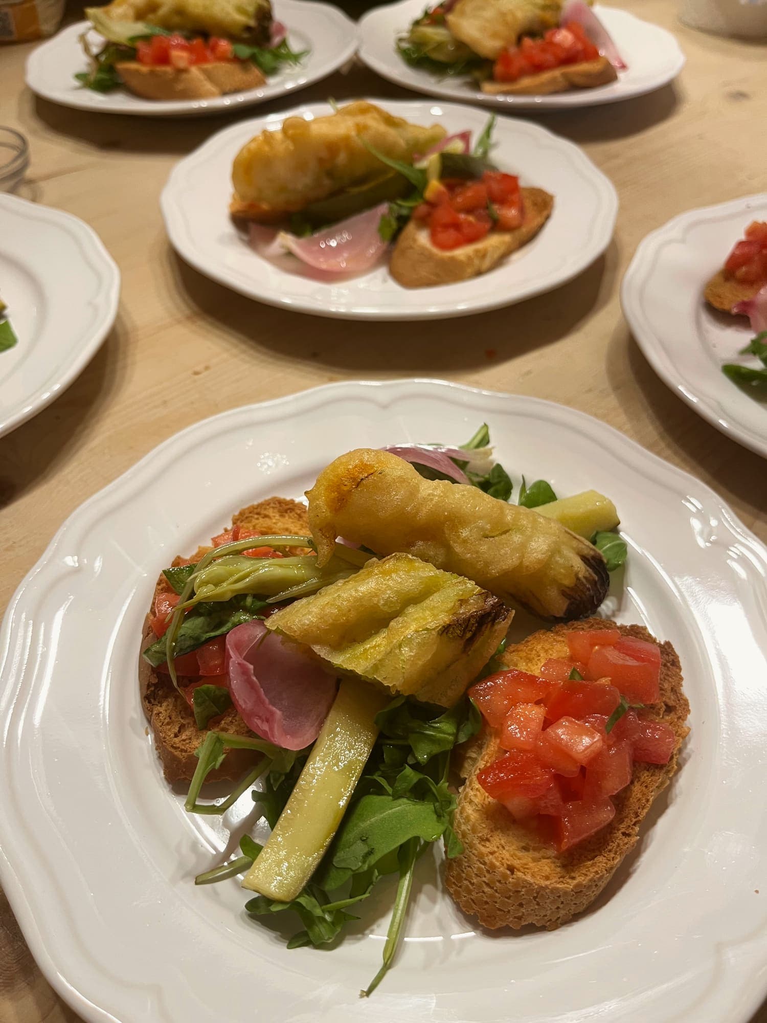 Fried zucchini flowers with toasted bread, chopped tomato and arugula, plated for the start of a dinner.