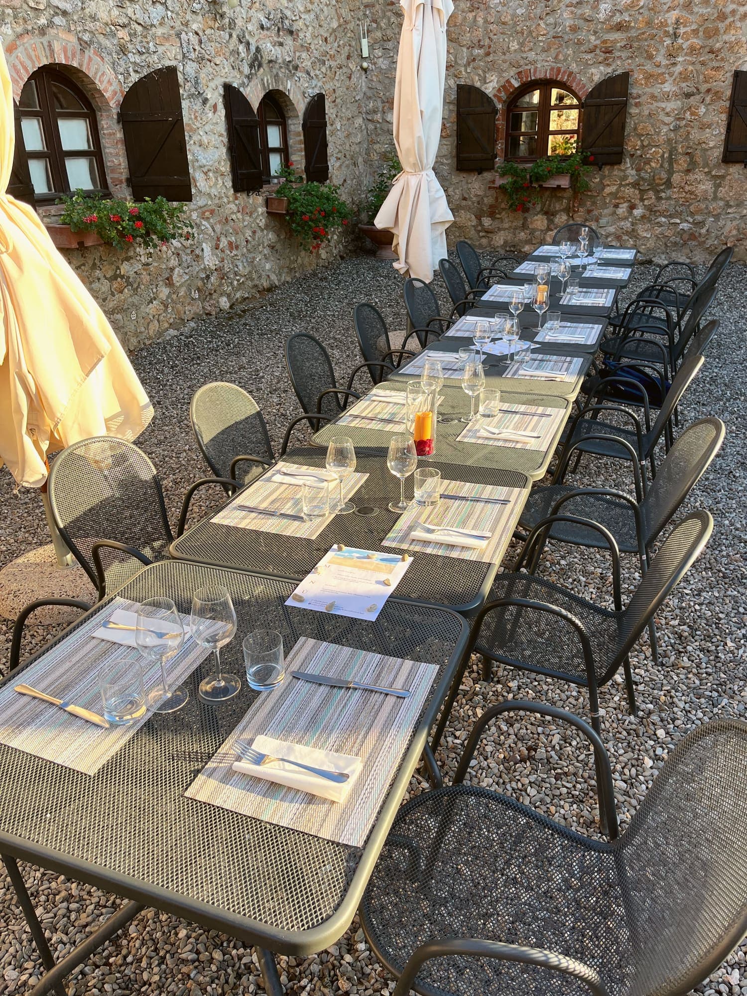 A long table laid for dinner in a stone courtyard, with glasses at every place and the parasols still closed.