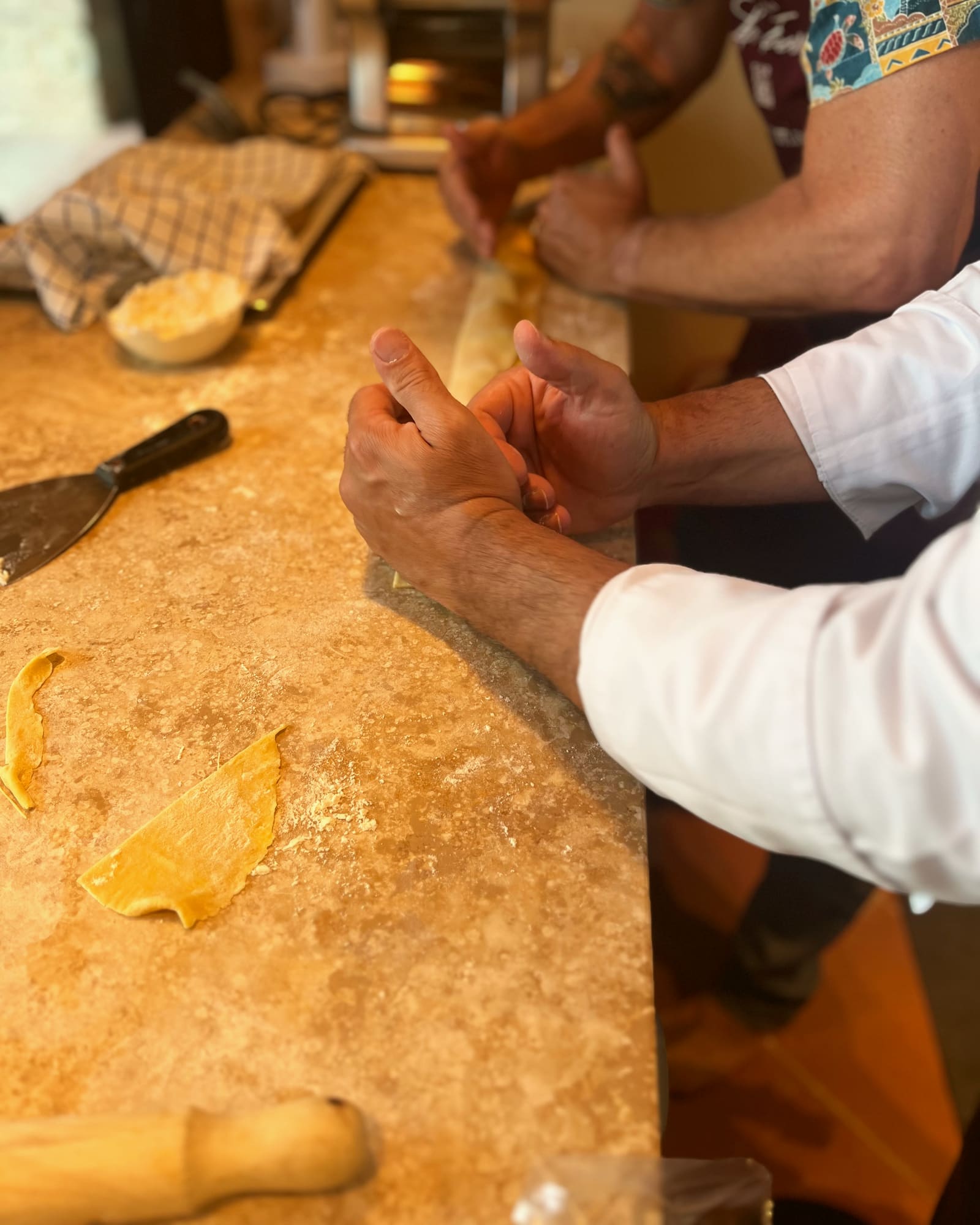 Hands shaping fresh pasta side by side along a long countertop during a cooking class in a villa kitchen