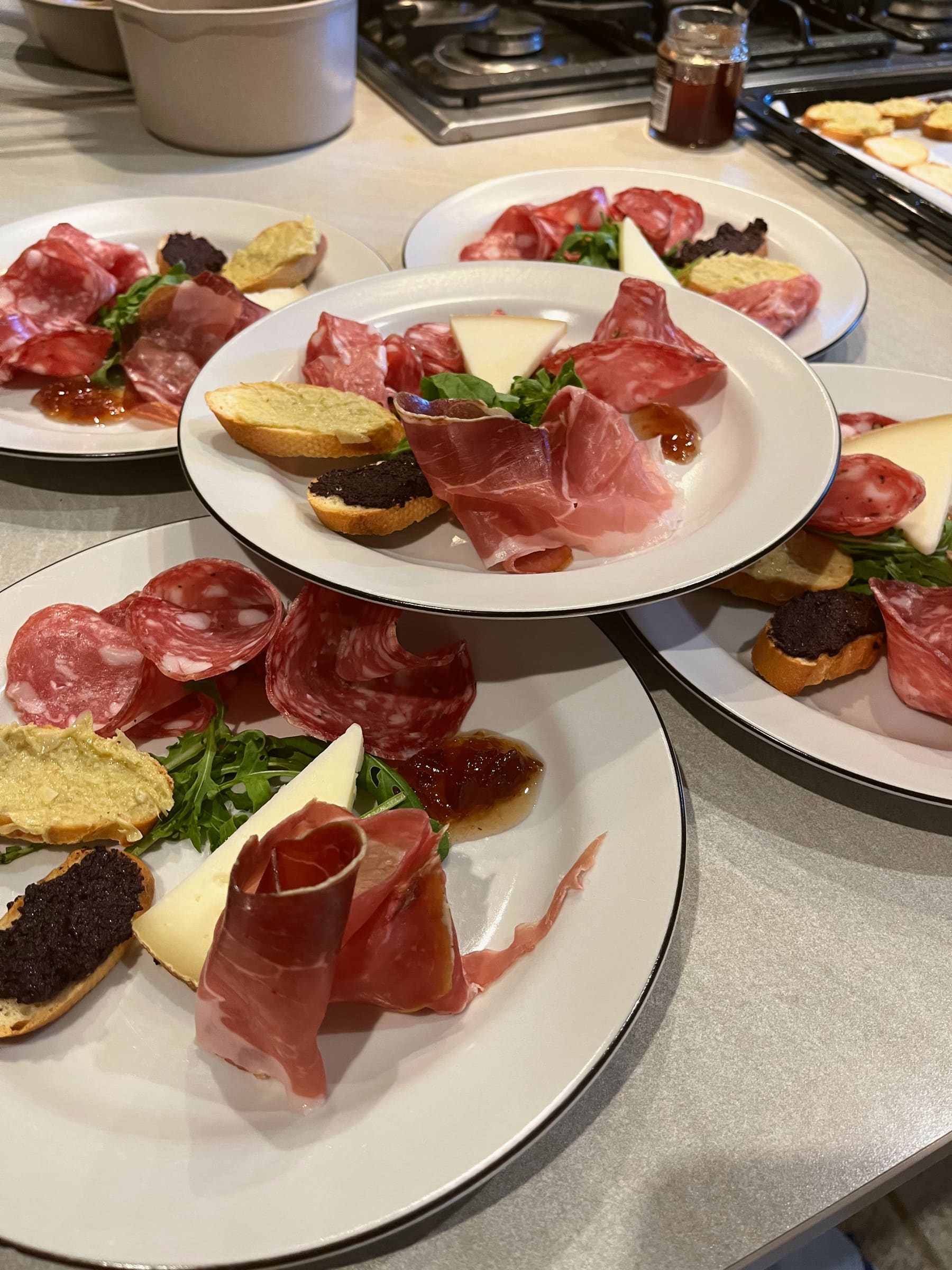 A gas stovetop and a plain countertop in a villa kitchen, with plated antipasti ready on the counter